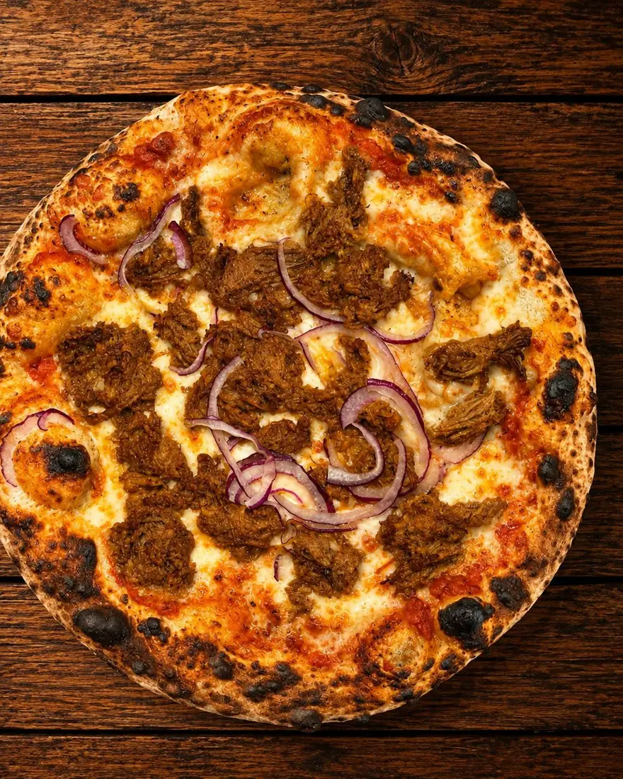 Pizza Cochinita: cochinita pibil, frijoles refritos y cebolla morada sobre masa de 48 horas